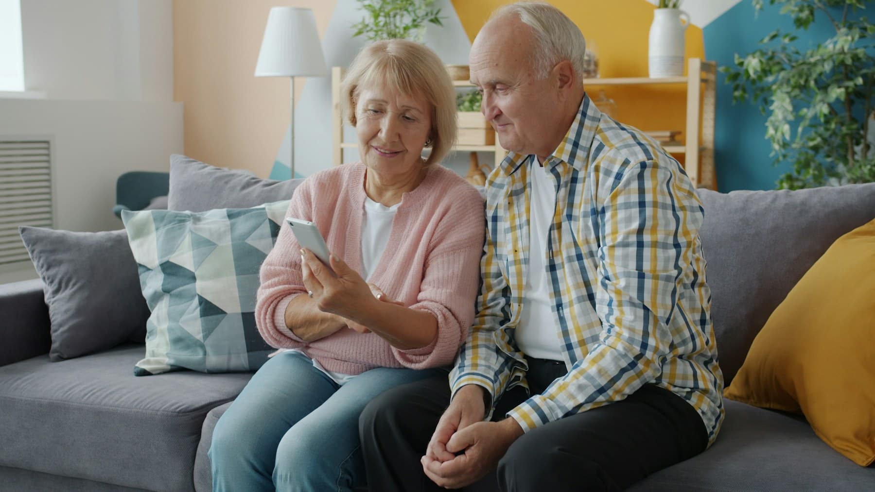Un couple de seniors regarde ensemble l'écran d'un téléphone, assis sur un canapé.